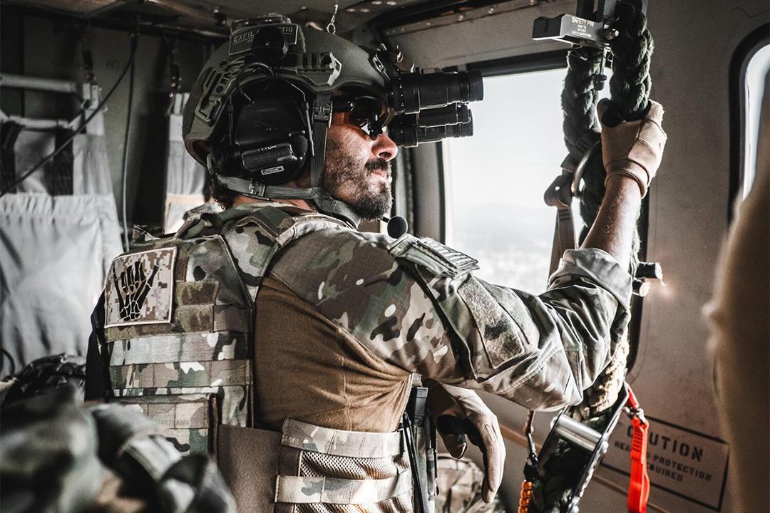 Image of man in army camo holding onto a rope in a vehicle