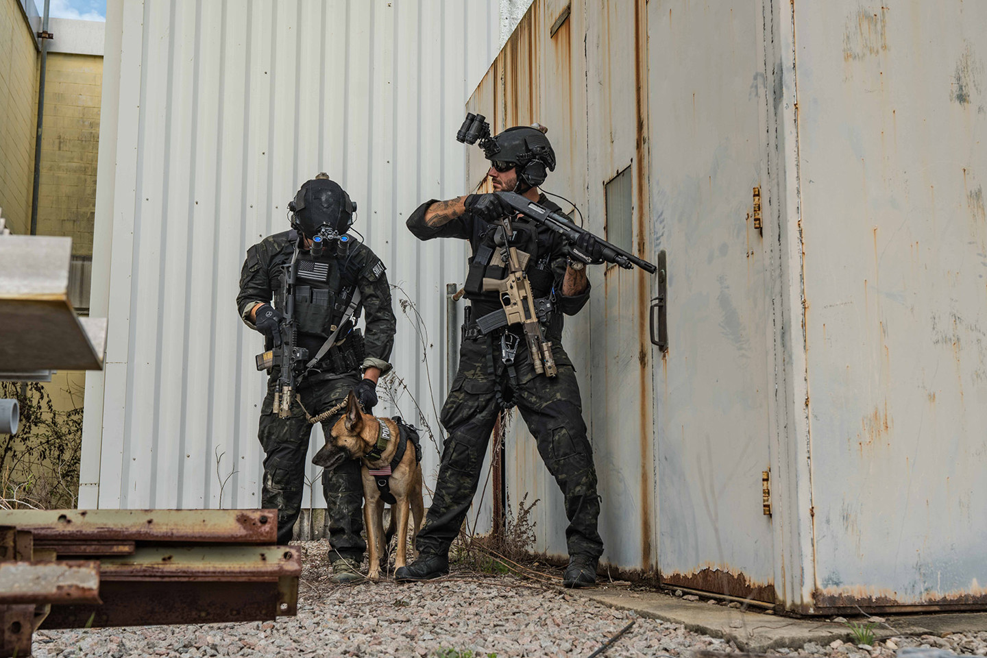 Two men in army camo with a dog holding guns