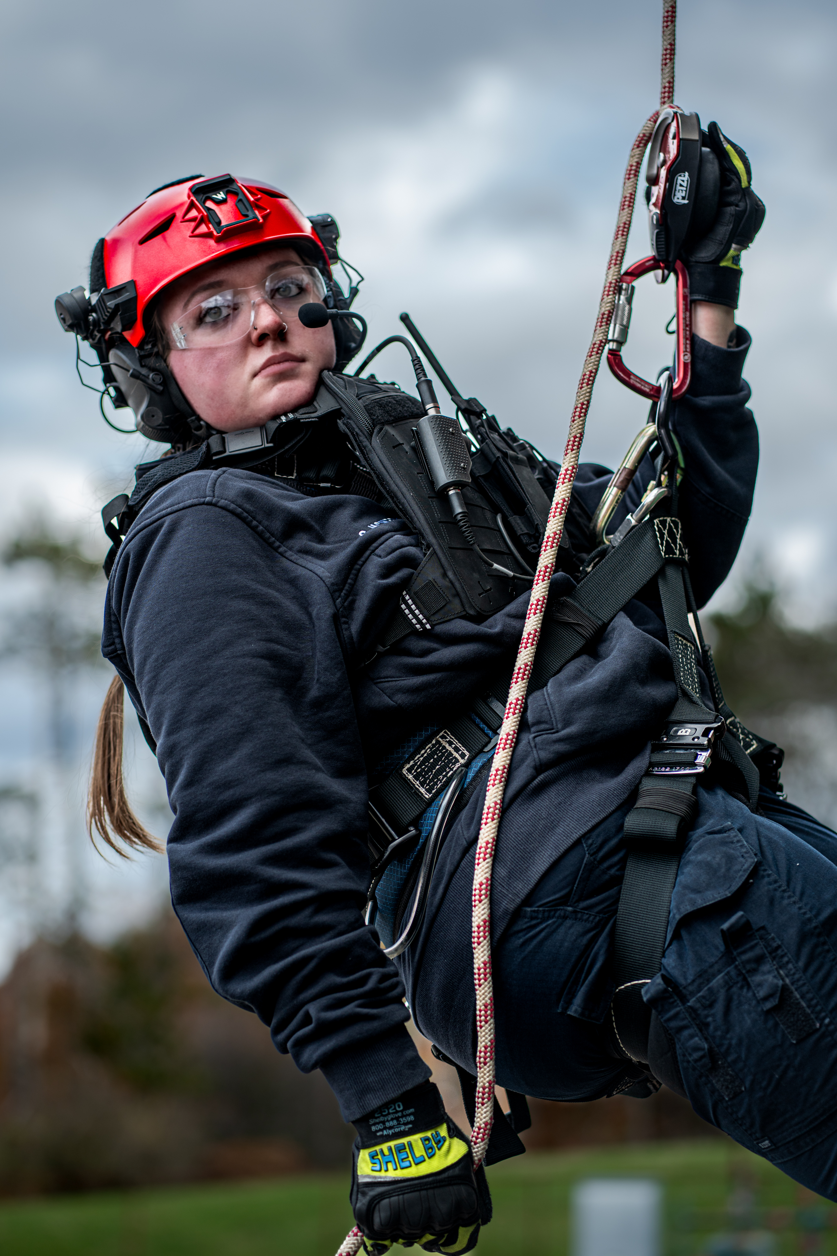 A woman is suspended in mid-air during a rope rescue wearing a red Team Wendy EXFIL Rescuer helmet. 