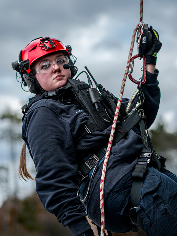 A woman is suspended in mid-air during a rope rescue wearing a red Team Wendy EXFIL Rescuer helmet.