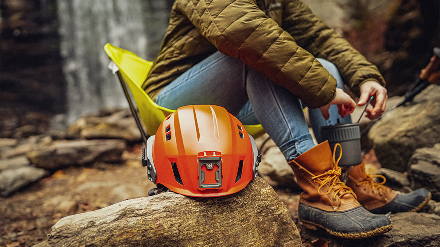 Image of orange helmet on log next to the legs of a person out of image