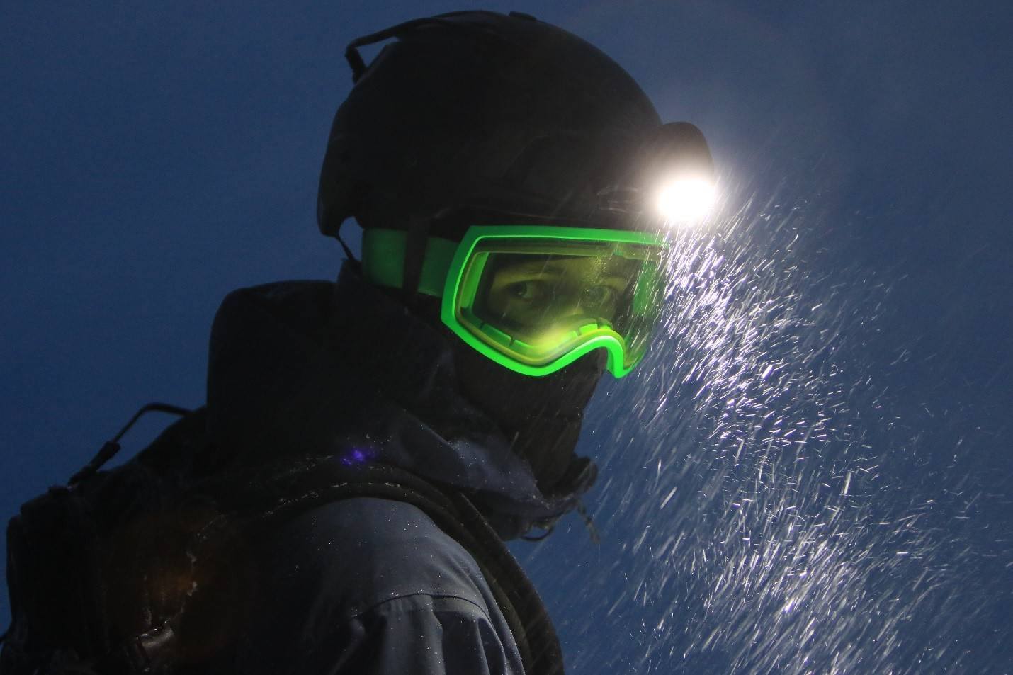 Man wearing headlight and helmet with neon green ski goggles