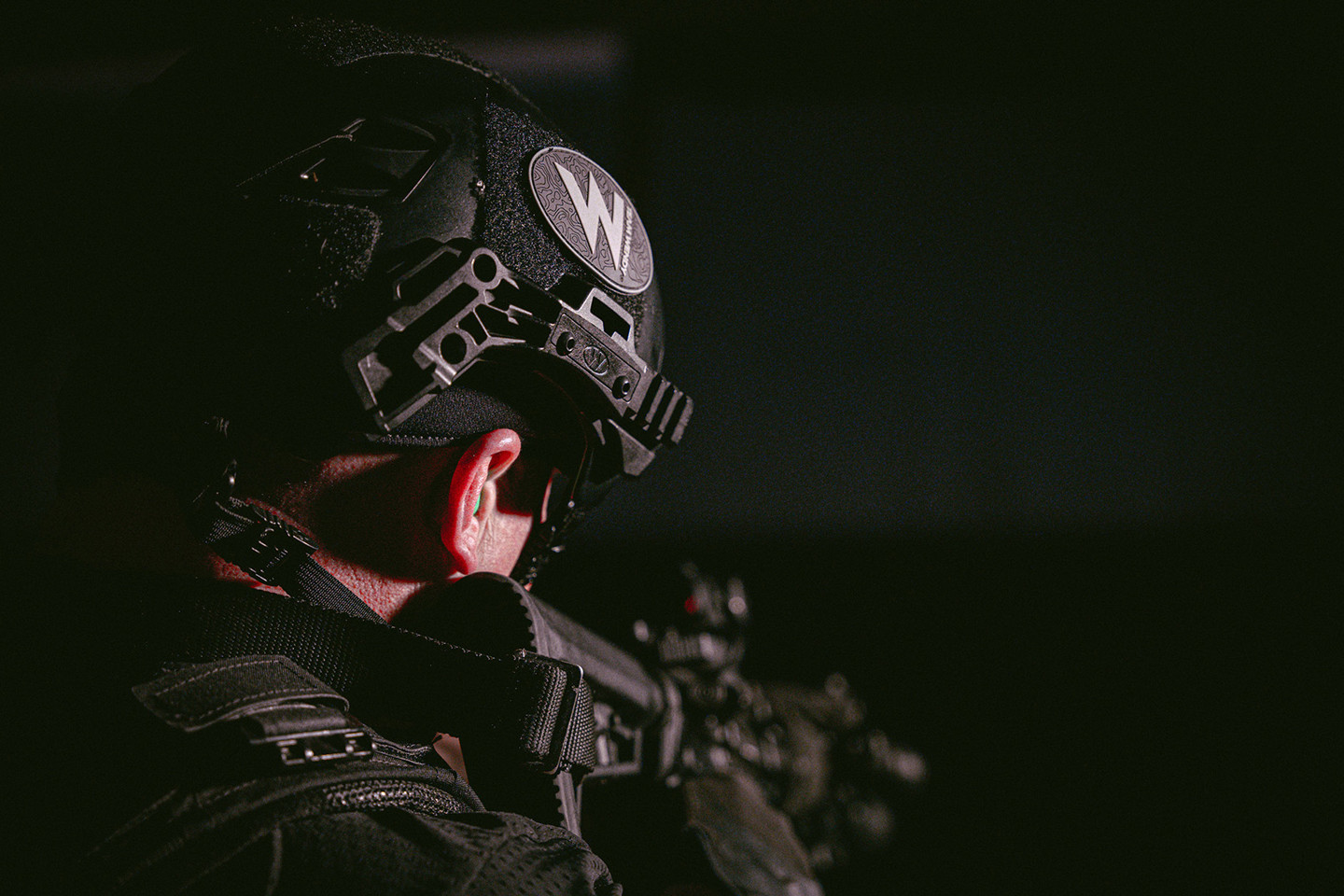 Close up image of the back of a man wearing a helmet and holding a gun