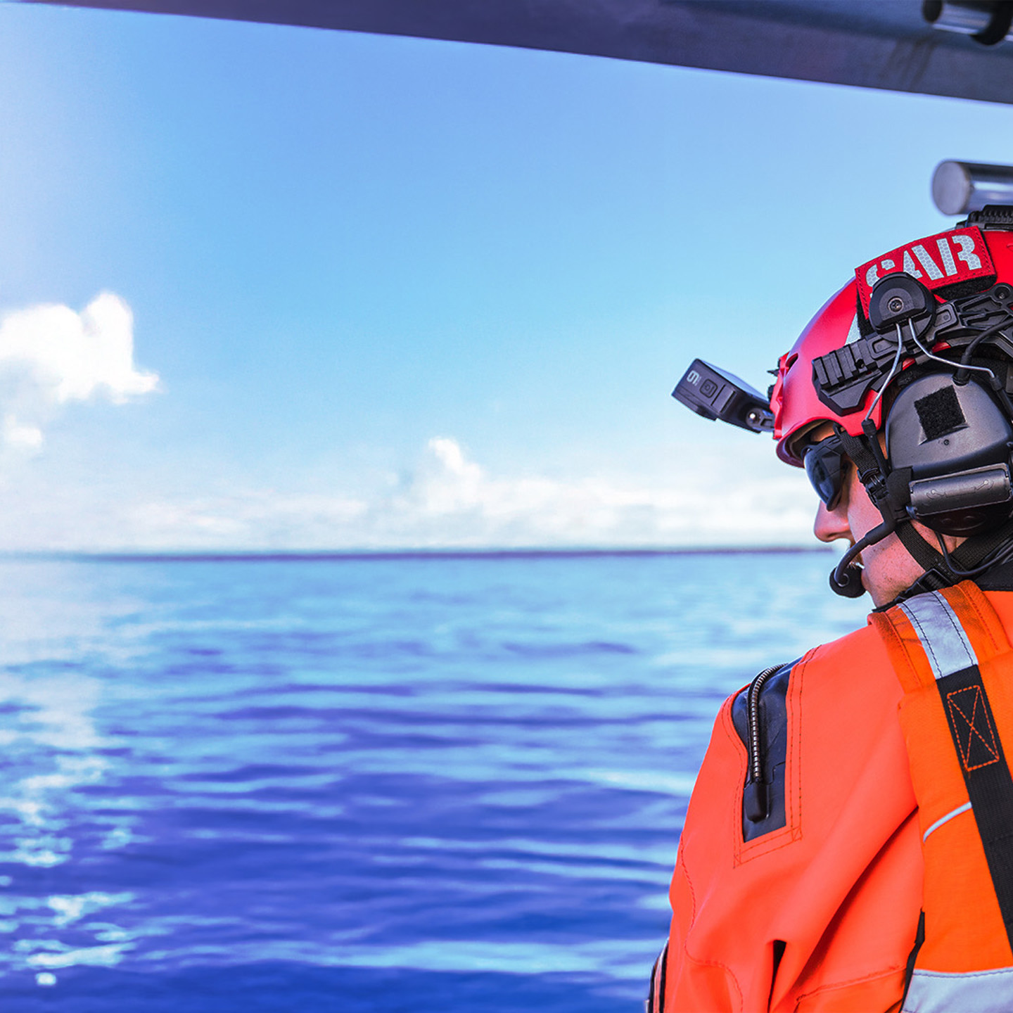 Image of man wearing an orange jacket and red Team Wendy helmet with a SAR patch, comms unit and headlamp on the water