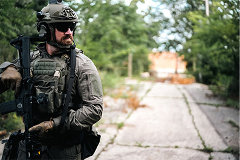 Man in camo, vest, and helmet holding a gun