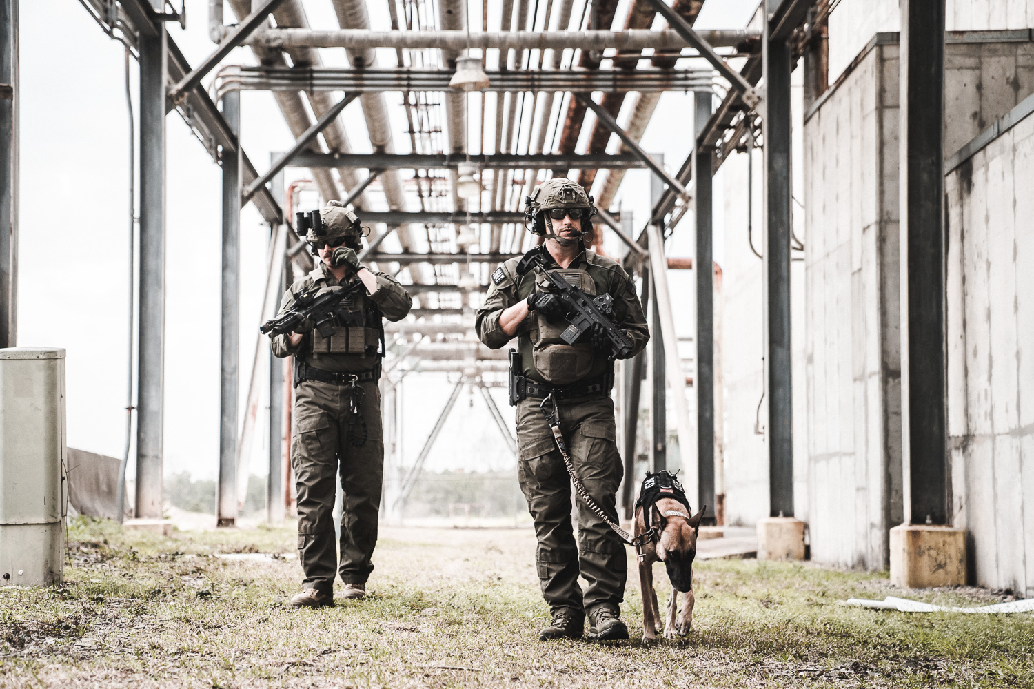 2 law enforcement officers wearing Ranger Green Team Wendy EXFIL Ballistic helmets patrol an area with their dog.