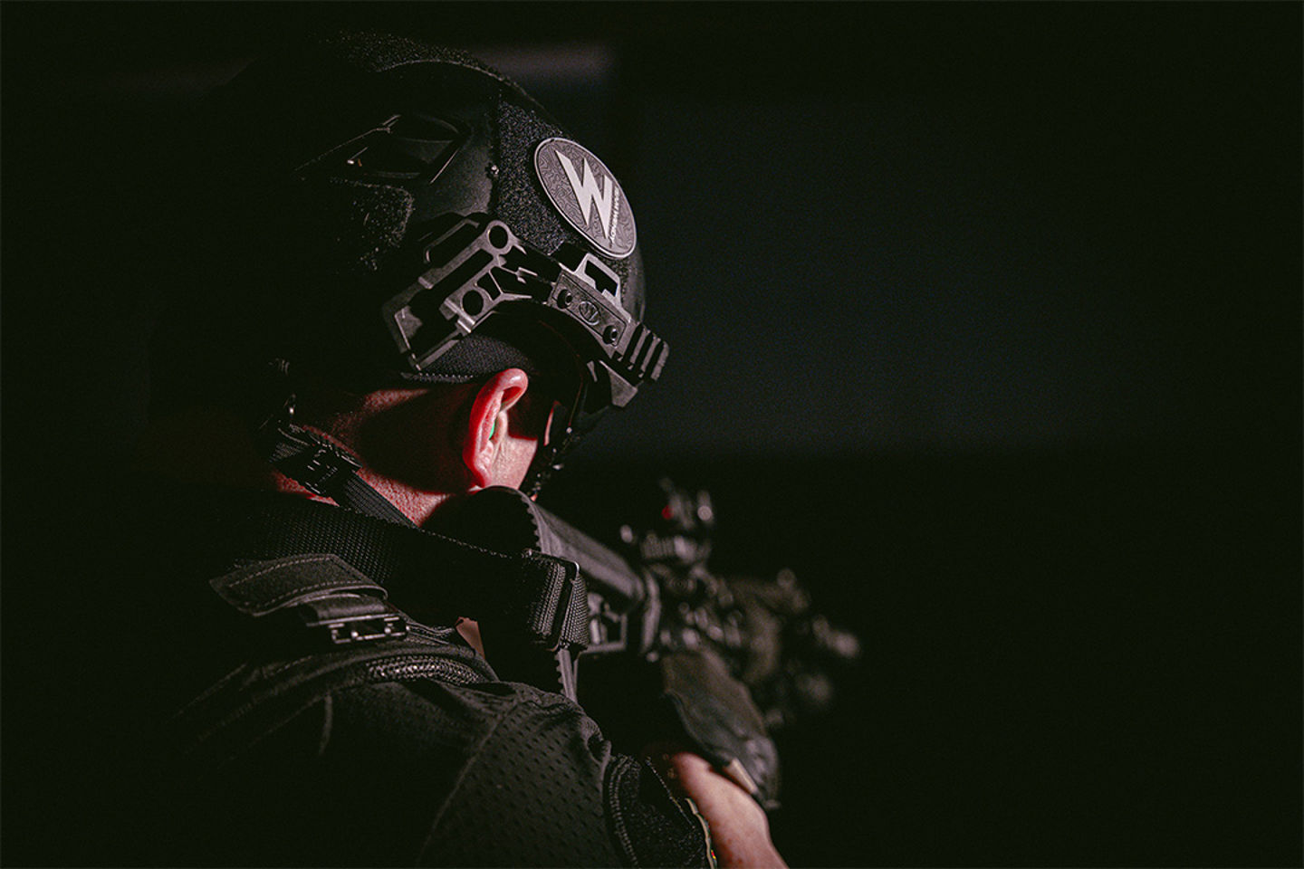 Image of the back of a man holding a gun and wearing a helmet