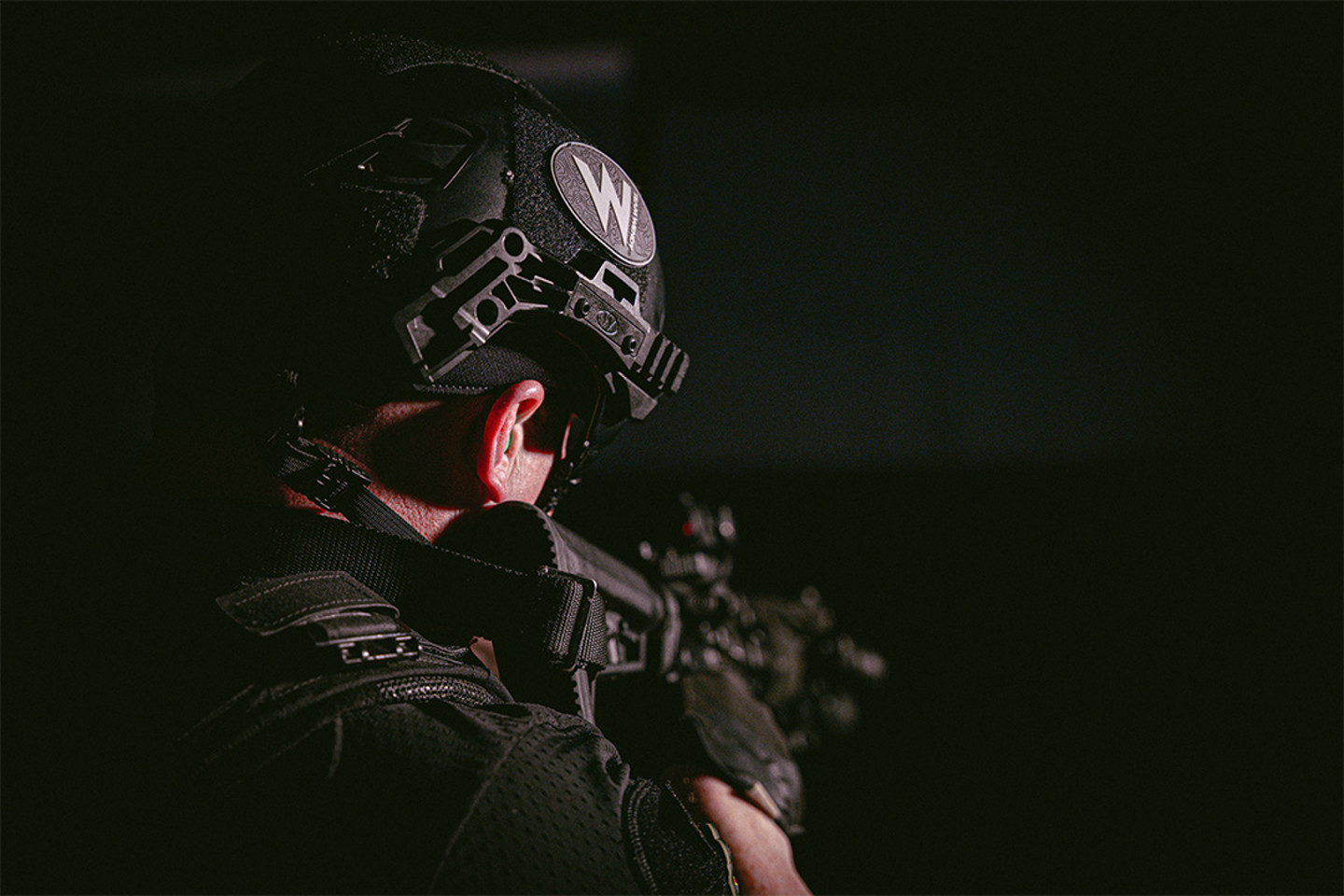Image of the back of a man holding a gun and wearing a helmet