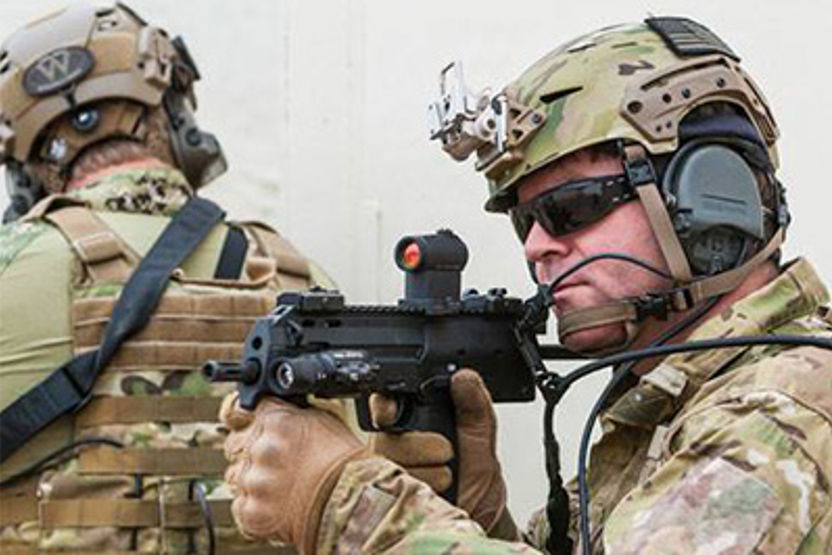 Homens vestidos com farda de camuflagem e capacete, empunhando uma arma