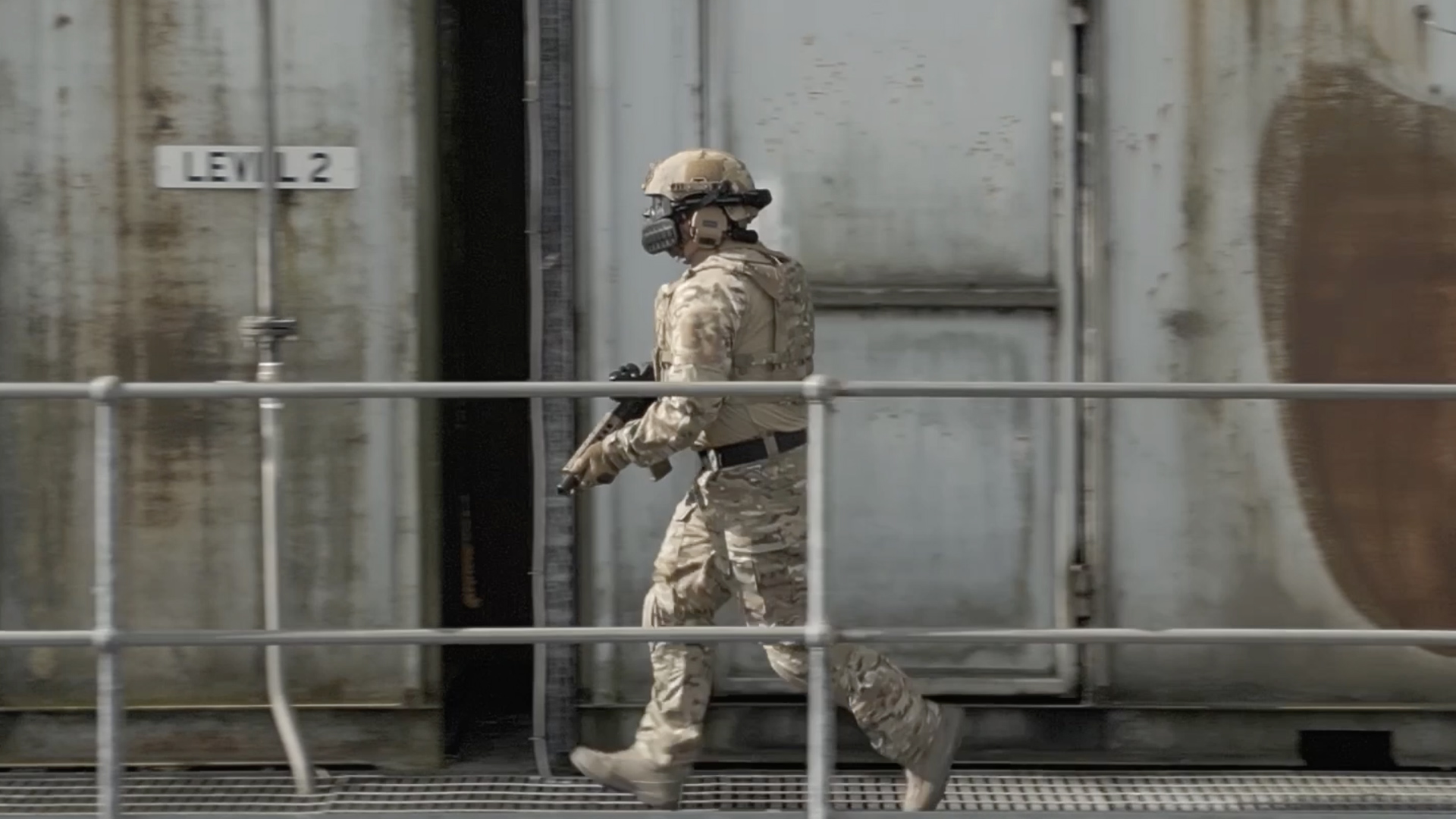 Soldier holding a gun walking next to a railing