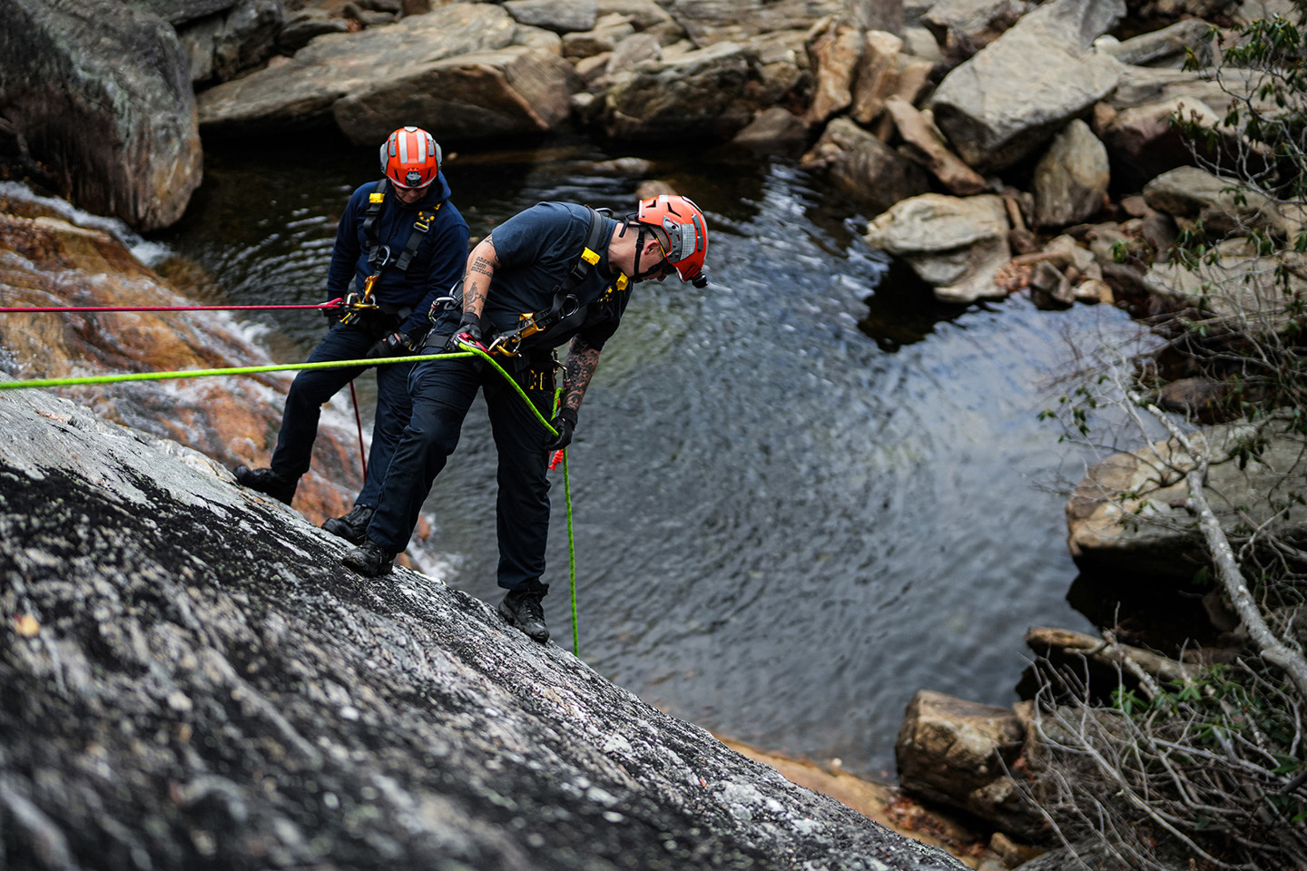 Two people with helmets on abseiling down cliff face