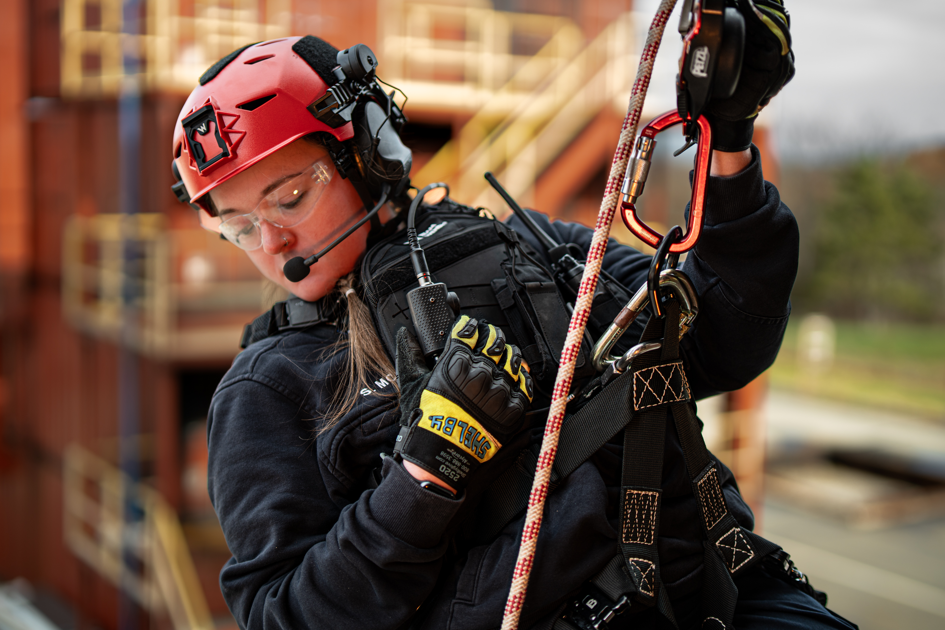 A woman is suspended in mid-air during a rope rescue wearing a red Team Wendy EXFIL Rescuer helmet. 