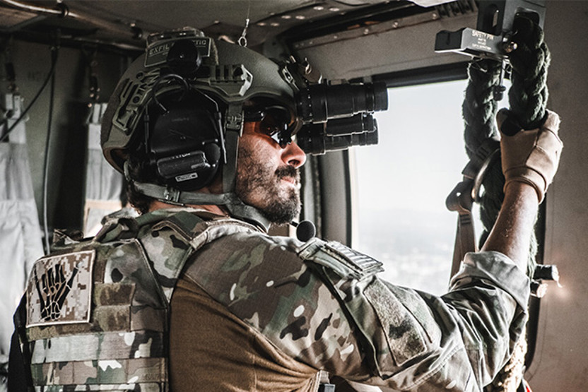 Man in green camo and helmet holding onto a rope