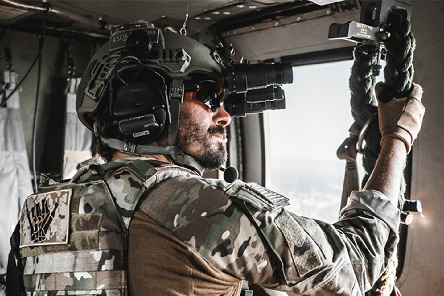 Man in green camo and helmet holding onto a rope