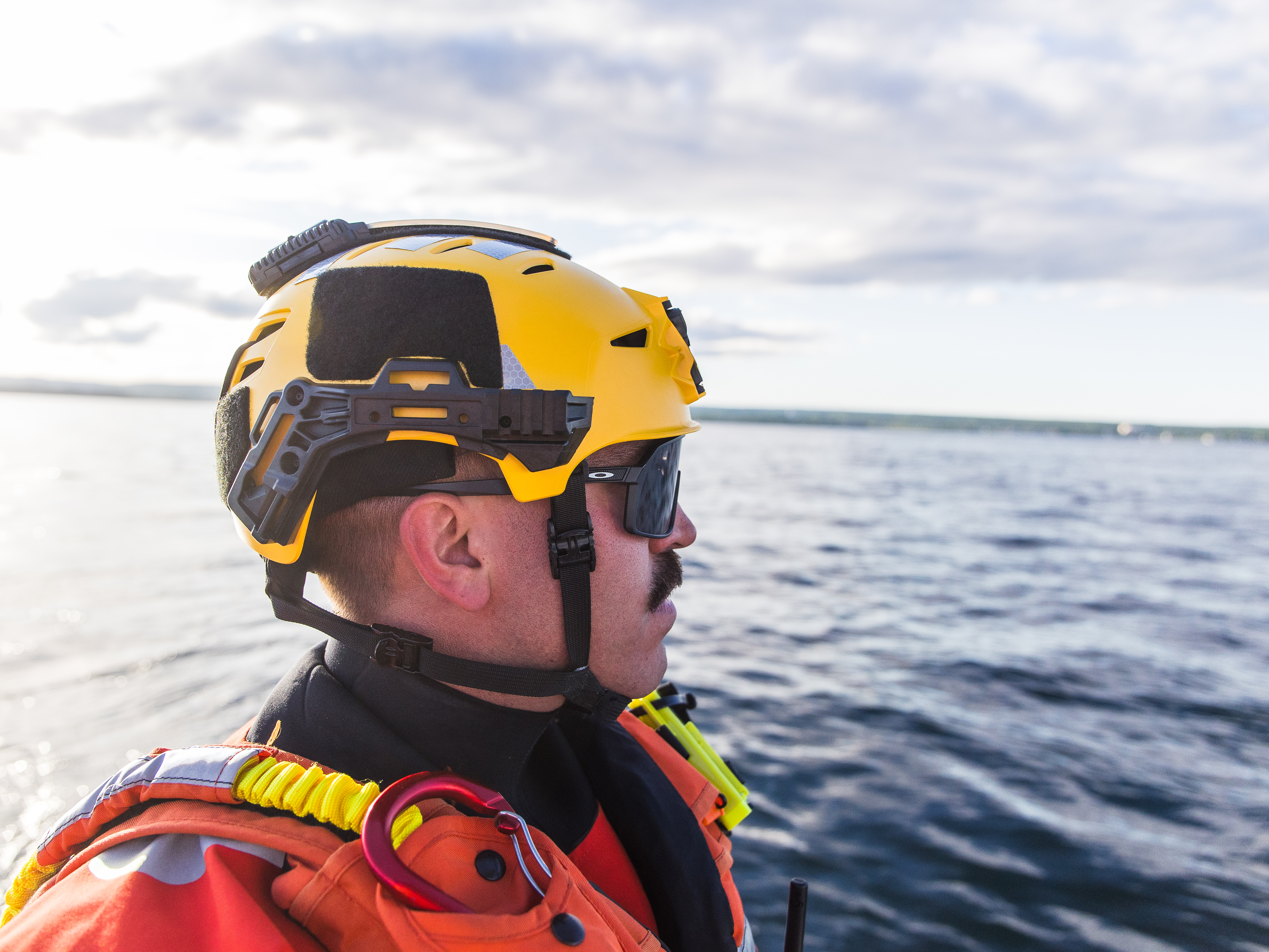 US Coast Guard on a boat surveying the area wearing a yellow Team Wendy EXFIL Rescuer helmet