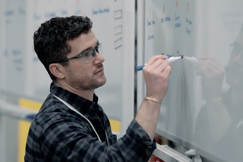 Man in safety goggles writing on whiteboard