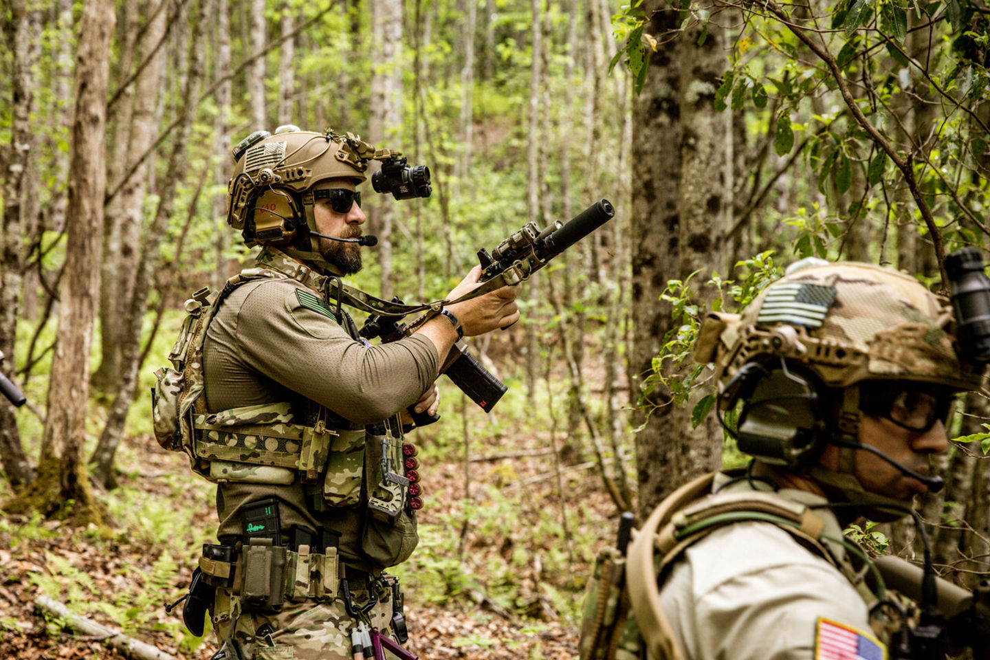 Deux hommes en tenue de camouflage et casqués, marchant dans la forêt, armés