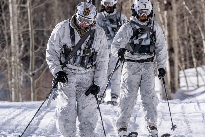 Men in snow wearing alpine camo uniform and helmets